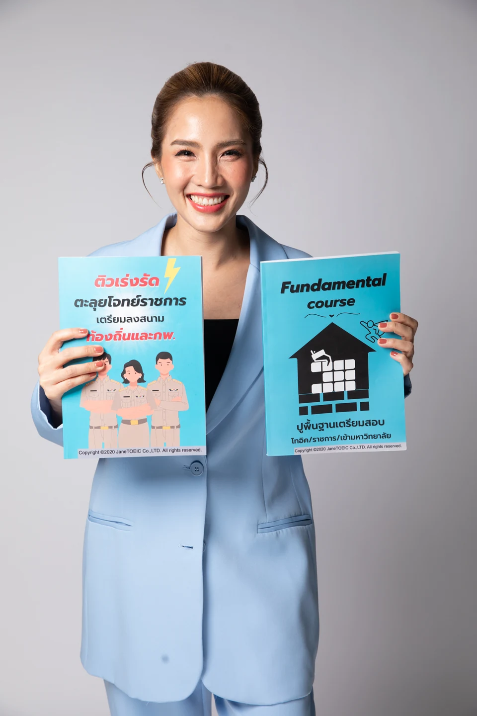 ครูเจนยิ้มและถือหนังสือคอร์สติวสอบสายราชการกับคอร์สปูพื้นฐานฉบับจริง